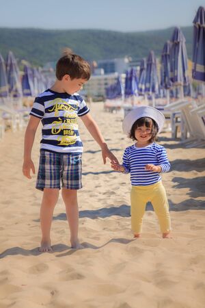 Two children in striped T-shirts are go on the beach near sun loungersの写真素材