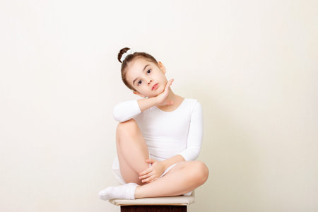 Beautiful little girl sits beautifully in a white dance swimsuitの写真素材