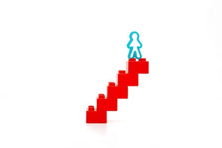 A blue man figurine stands on top of a red staircase. White background. Isolated.Business concept career growth and success.の写真素材