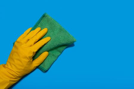 Hand in yellow glove with green rag of microfiber wipes on blue background. Copy space. Horizontalの写真素材