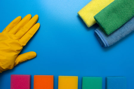 A hand in a yellow rubber glove, three colorful, dry microfiber cloths and rainbow colored sponges...