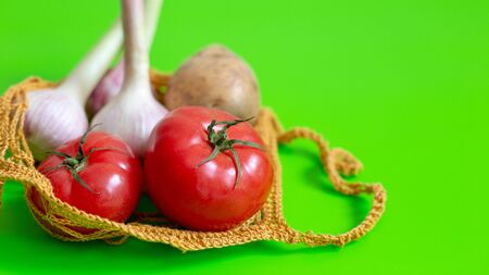 Knitted bag on a green table with vegetables: tomatoes, garlic, potatoes. Vegetarian Vegetables. Healthy Food. Copy space. Close up. Wideの写真素材