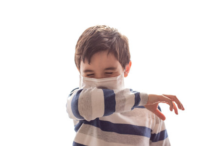 A boy with closed eyes sneezes or coughs into his elbow on white background.