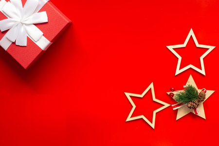 A red gift box with a white bow, wooden Christmas tree decorations in the form of stars on a red...