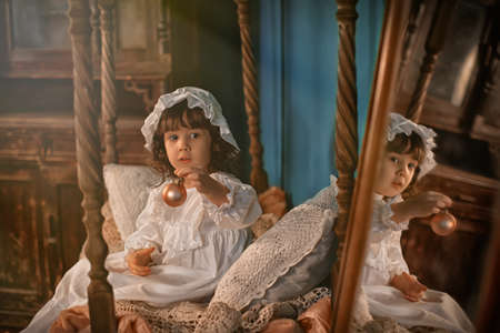 A lovely little girl in a white cap sits in a white vintage night dressの写真素材