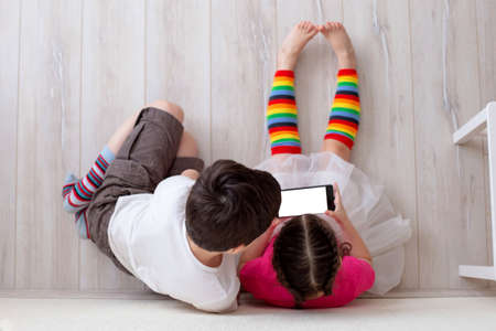 Two children, boy and girl, are sitting on the floor and playing on a smartphoneの写真素材