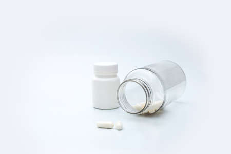 A transparent bottle lies on a white background, a white bottle of pills and several white capsulesの写真素材