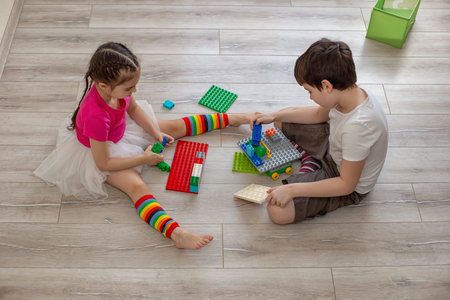 Two children, a boy and a girl, sit on the floor in room and play in plastic constructionsの写真素材