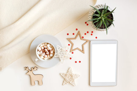 A digital tablet with a blank screen lies on a white table surrounded by flat wooden Christmas...