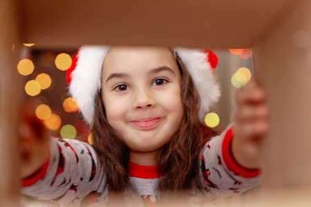 A happy girl in a Santa Claus hat takes a present out of the boxの写真素材