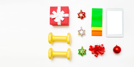 Dumbbells, set of elastic bands, gift box, tablet computer and Christmas decorations on a white...