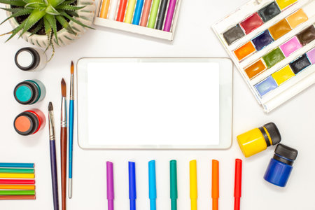 White digital tablet with a blank screen on a white table and drawing supplies
