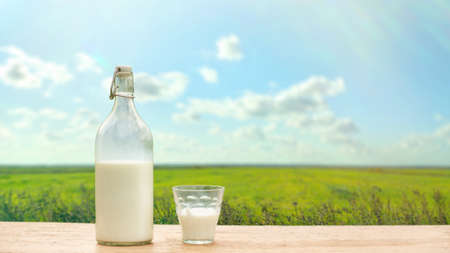 Bottle and glass with fresh milk on a background of green meadow and blue skyの写真素材