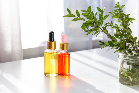 Two bottles of yellow and a bottle of pink cosmetic organic oil, stand on a white table