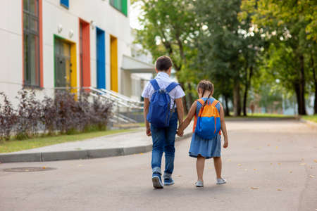 two schoolchildren, a little girl and a boy in a with backpacks go on the way to school.の写真素材