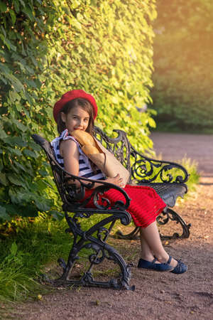 beautiful brunette girl sits on a bench, holding a French baguettesの写真素材