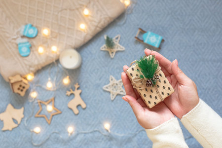 A small Christmas present in womens palms, on a background of a blue knitted plaid