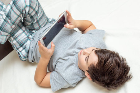 boy lies on his back playing digital tabletの写真素材