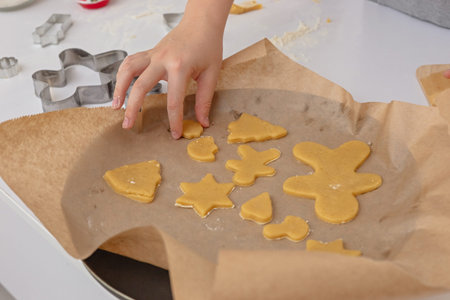 One Childrens hand lays dough figurines in the form of Christmas symbols on parchment