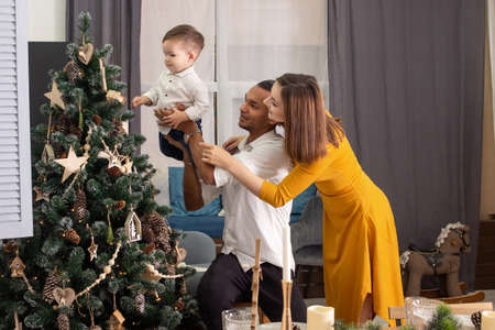 Happy young family show son a Christmas tree with wooden toys and decor in eco styleの写真素材