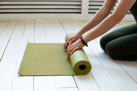 Young slender womans hands twisting green mat for fitness or yoga on white wooden floor.の写真素材