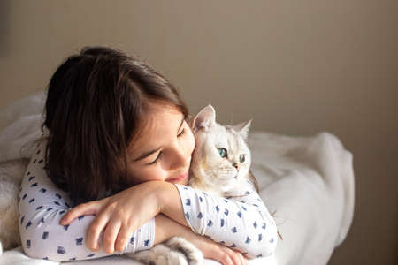 The little girl lies with a white cat on the bed, hugs himの写真素材