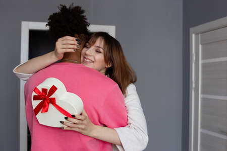 A beautiful girl, hugging her boyfriend , holds a white box in the form of a heart with a bow in her handsの写真素材