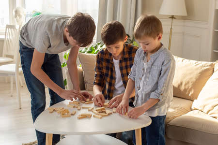 Three boys, in home enthusiastically play a board game made of wooden rectangular blocksの写真素材