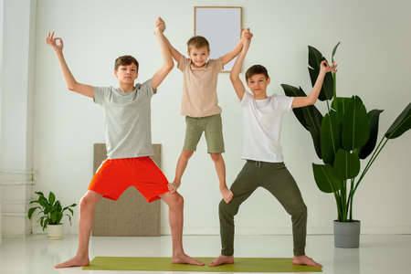 a happy boy and two teenagers perform group yoga exercises with support while sitting on a sports mat.の写真素材