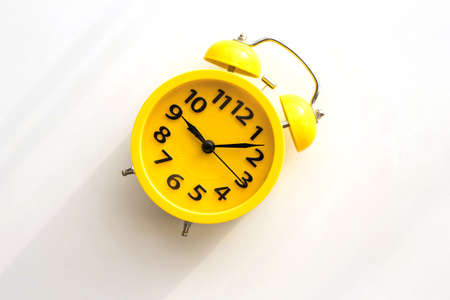 A yellow retro alarm clock with a black dial lies on a white table diagonally to the left.の写真素材