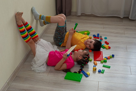 A boy and a little girl, lie on the floor, on their backs, play merrily with a multicolored plastic...