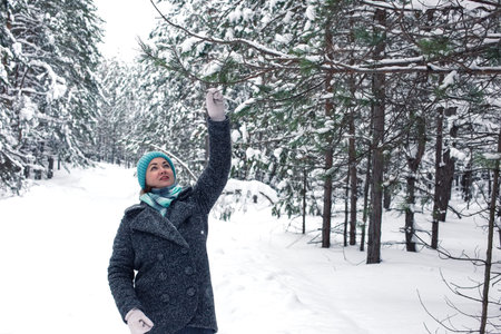 A happy woman in a winter snow-covered forest, holding a pine branch