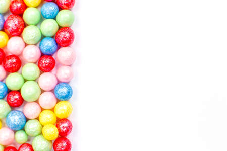Multi-colored round glossy balls of sugar confectionery topping lie at the left on a white background.の写真素材