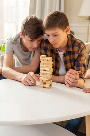 A two teen boys are enthusiastically playing a board game made of wooden rectangular blocksの写真素材