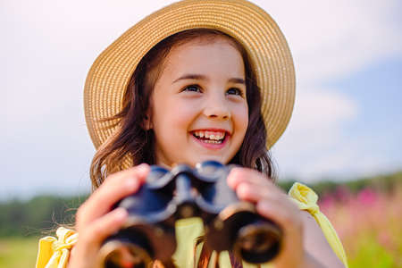 Happy cute little girl 4-5 years old stands in nature , holds binocularsの写真素材