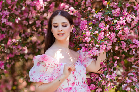 A girl in a pink dress standing near pink blooming apple treesの写真素材