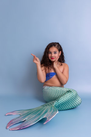 A happy girl in a mermaid costume sits on a blue backgroundの写真素材