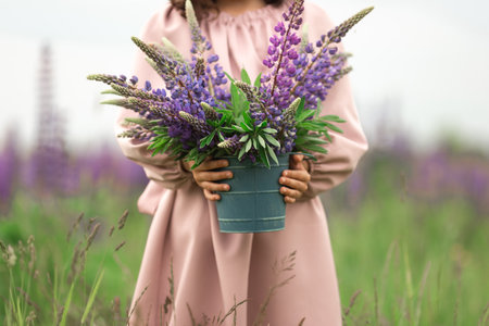 Young female holding lupine bouquet in flower field with pink dressの写真素材