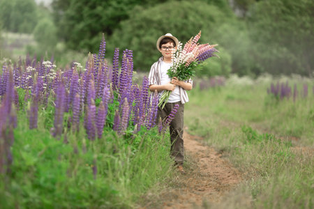 Young caucasian boy holding lupine flowers in lush green fieldの写真素材