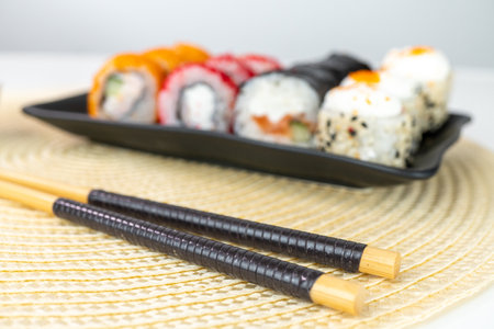 Variety of sushi rolls on black plate with chopsticks on woven matの写真素材