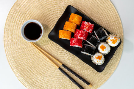 Assorted sushi rolls with soy sauce on black plate and woven matの写真素材