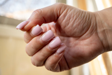 a hand with an outgrown acrylic or gel manicure in a soft pink shadeの写真素材