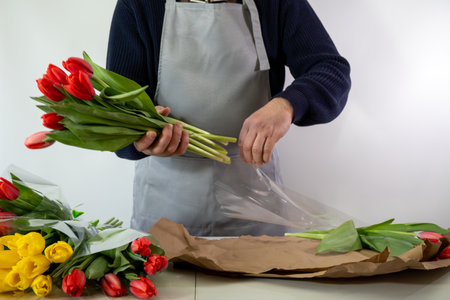 Adult caucasian male florist arranging tulips with care in a flower shopの写真素材