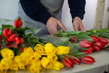 Adult caucasian male arranging red and yellow tulip bouquets on counterの写真素材