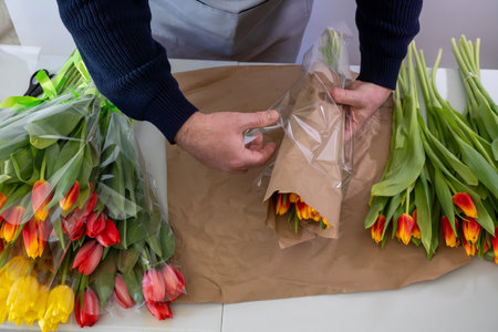 Male florist wrapping tulips in shop with colorful bouquets and craft paperの写真素材