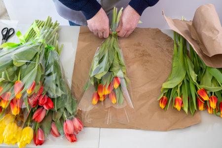 Caucasian male adult arranging vibrant tulip bouquets on craft paperの写真素材