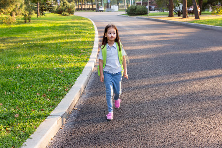 Young girl walking on park pathway with backpack in sunny weatherの写真素材