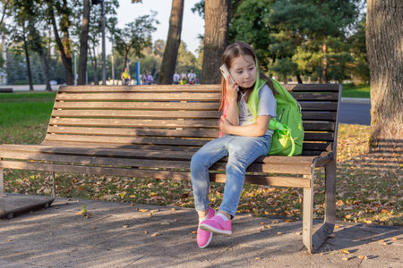 Young girl with backpack sitting on park bench in autumn afternoonの写真素材