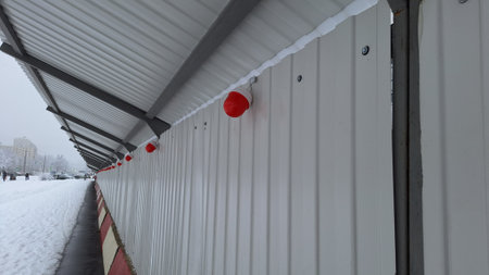 Snowy urban walkway with red lights and corrugated metal roofの写真素材