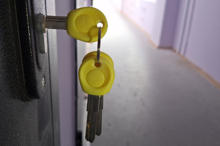Yellow plastic-headed keys in lock on dark doorway in hallway settingの写真素材